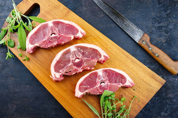 Wall Mural - Raw lamb saddle back chop steak with herbs offered as top view on a wooden design board