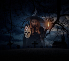 Halloween Witch Holding A Skull Standing Over Grass, Dead Tree, Cross, Birds With Church Over Spooky Cloudy Sky, Halloween Mystery Concept