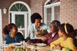 © Drazen - Happy black multi-generation family enjoys at dining table on patio.