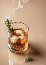 Whiskey In Cristal Glass With Rosemary And Beautiful Swirls Of Smoke On Brown Monochrome Background. Close Up, Text Space