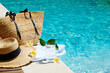 © Evrymmnt - Swimming pool essentials concept. Beach bag with items for safe sunbathing on the deck, sunglasses, straw hat, white blanket & sunscreen product. Flat lay, copy space, top view, background.