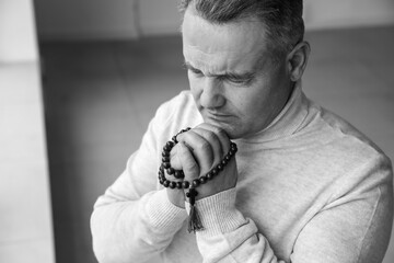 Religious mature man with cross praying in room, black and white effect