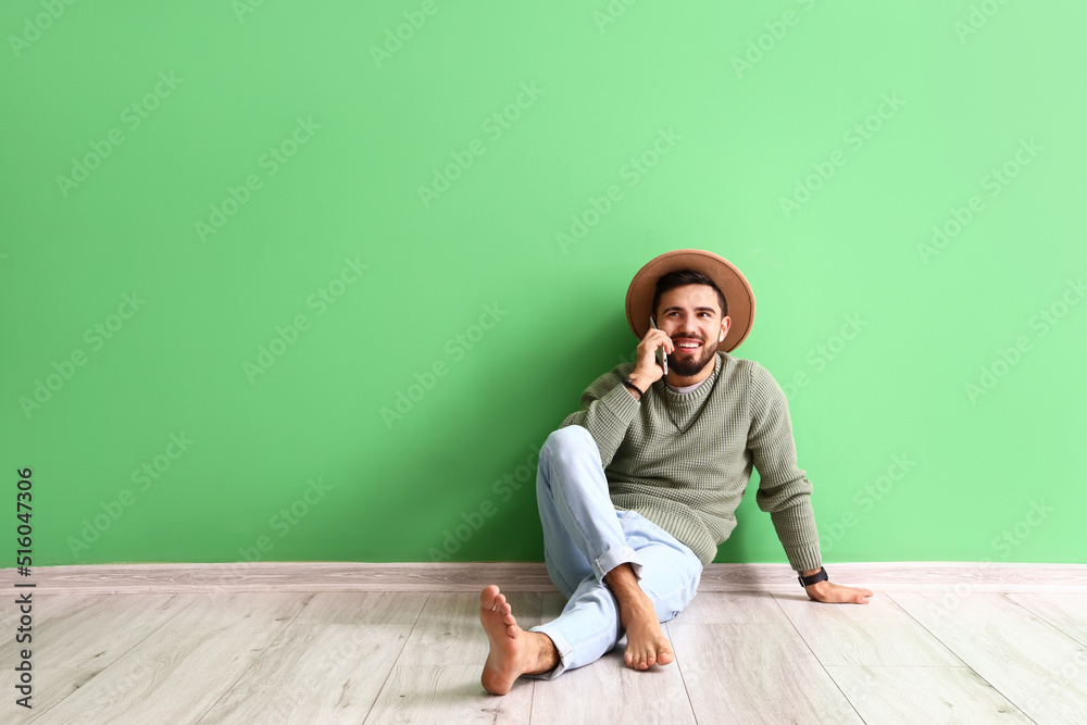Handsome barefoot man talking by mobile phone near green wall