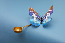 Blue Butterfly Siting On Golden Spoon And Kipping Balance On Blue Background.