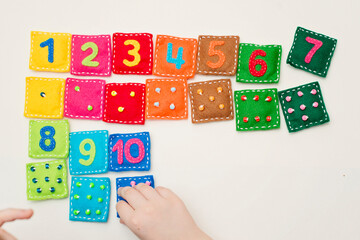 toddler playing on the floor. Home made game: find the right pair. Different color stuffed felt square with numbers and matching domino style dots. Early education, learning numbers.