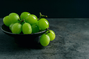 a branch of green juicy grapes in a plate with copy space. black background. front view. place for w