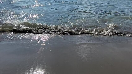 Sticker - Glittering sea waves water on the beach with volcanic sand.