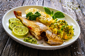 Fried perch with lemon and salad served on wooden table
