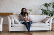 © fizkes - In cozy living room African woman with little daughter spend leisure on internet using modern smartphone. Vlogging, new cool amusing mobile application usage, video games for kids development concept