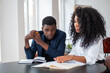 © ImageFlow - Two african business people working together, looking at notebook on desk