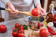 woman blanching a tomato holding over pan with hot water for further peeling
