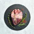Raw pork heart on a black stone plate with spices and herbs. Meat. On a stone background.