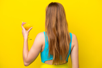 Young caucasian woman holding a cocktail isolated on yellow background in back position