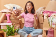 Relocation and tenancy concept. Funny woman makes grimace fish lips shows peace gesture takes selfie via smartphone rents new house moves in surrounded by cardboard boxes with household items