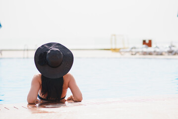 Vacation lifestyle scene of young woman sitting in swimming pool in morning time. Weekend and holiday lifestyle concept