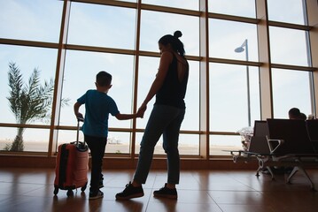 Family at airport before flight. Mother and son waiting to board at departure gate of modern international terminal. Traveling and flying with children. Mom with kid boarding airplane. yellow family