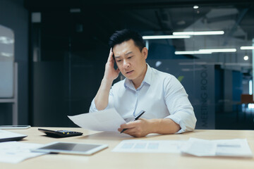 Wall Mural - Thinking Asian businessman working in office on documents, man thinking and reading letter from bank