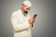 Happy indian pakistani muslim man using smartphone, online shopping, internet banking, using app, watching cricket match, Entertainment, Technology, Social media.  Isolated over grey background. 
