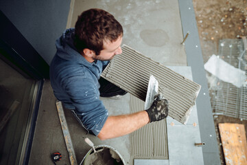 Laying Ceramic Tiles. Worker placing ceramic floor tile in position over adhesive.