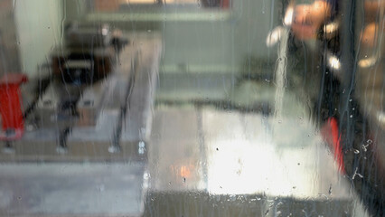 Worker is washing plant mill machine using a metal water sprayer. View from stained glass.