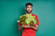 Young African man looking frustrated while holding a bunch of lettuce against green background