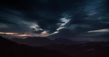 Late evening timelapse of cloudy sky in mountains landscape at sunset. Hyperlapse footage of clouds moving on the sky after stormy rain with city light on background
