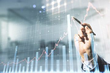 Man hand with pen working with abstract virtual financial graph on blurred office background, financial and trading concept. Multiexposure