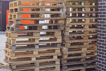 a row of brown wooden pallets stand on the street against the brick wall of the building