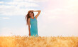 Happy woman enjoying the life in the field. Nature beauty, blue sky, white clouds and field with golden wheat. Outdoor lifestyle. Freedom concept. Woman walk in summer field