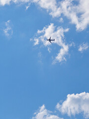 Wall Mural - The passenger airplane is flying far away in the blue sky and white clouds. Aircraft in the air. Light vertical background or illustration about international passenger air transportation