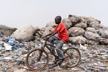 a poor african slum boy cycles through the city's garbage dump in search of spare tires