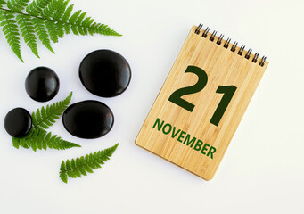 November 21. 21th day of the month, calendar date. Notepad, black SPA stones, green leaves. Autumn month, day of the year concep