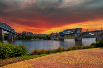 Wall Mural - the Walnut Street Bridge and the Chief John Ross Bridge over the rippling blue waters of the Tennessee River surrounded by lush green trees with powerful red clouds at sunset at Coolidge park