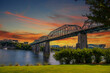 the majestic Walnut Street Bridge over the rippling blue waters of the Tennessee River surrounded by lush green trees and buildings with powerful clouds at sunset at Coolidge park in Chattanooga