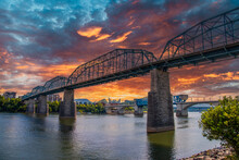 The Majestic Walnut Street Bridge Over The Rippling Blue Waters Of The Tennessee River Surrounded By Lush Green Trees And Buildings With Powerful Clouds At Sunset At Coolidge Park In Chattanooga