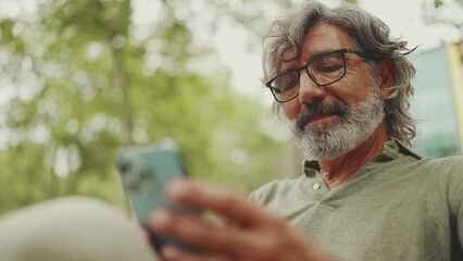 clouse-up, positive middle-aged man with gray hair and beard wearing casual clothes sits on bench an