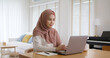 © ChayTee - Young Gen Z workforce islam woman self learn MBA online class reskill upskill job at home. Asia people arab girl study relax sit at table wear hijab scarf write or typing e-mail work on digital laptop