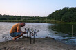 Fisherman with carp fishing rods and carp bite indicators and reels set up on rod pod near river on nature in the evening