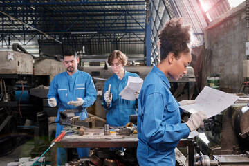 Young African American female industry worker works with mechanical drawing and metalwork precision tools, lathe machines, and spare parts workshop with multiracial team in a manufacturing factory.