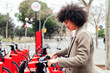 young latin woman taking a bike from a rental station, active lifestyle and sustainable mobility concept