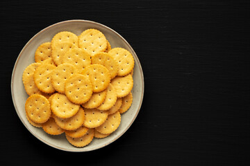 Wall Mural - Salty Round Crackers on a Plate on a black surface, top view. Flat lay, overhead, from above. Copy space.