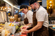 © Westend61 - Chef preparing food by colleague in restaurant kitchen