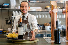Smiling Bartender With Wine Bottle And Chips At Bar Counter