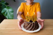 Senior Woman With Birthday Cake Sitting At Table