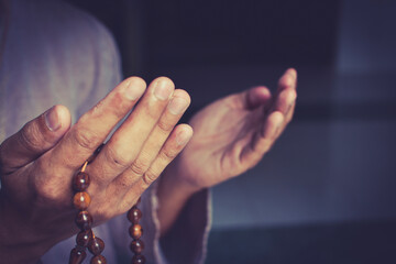 Muslim man in brown session lift two hand for praying and wearing bead on hand to determine the number of prayer services.concept for Ramadan, Eid al Fitr, eid ad-ha, meditation, islamic praying