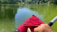 Kayaker point of view while paddling and exploring in his red kayak over a green still  waterl river in SE Spain.