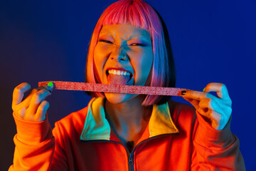 Wall Mural - Asian girl with pink hair making fun while eating chewing marmalade