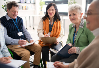 Wall Mural - Excited elderly people attending group therapy session at nursing house, positive senior man and woman sitting in circle, having conversation with psychologist