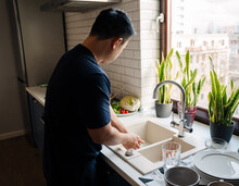 Adult Brunette Asian Man Wearing T-shirt Washing Dishes At Kitchen