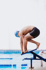 Wall Mural - latin teenager man swimmer athlete wearing cap and goggles in a swimming training holding On Starting Block In the Pool in Mexico Latin America	